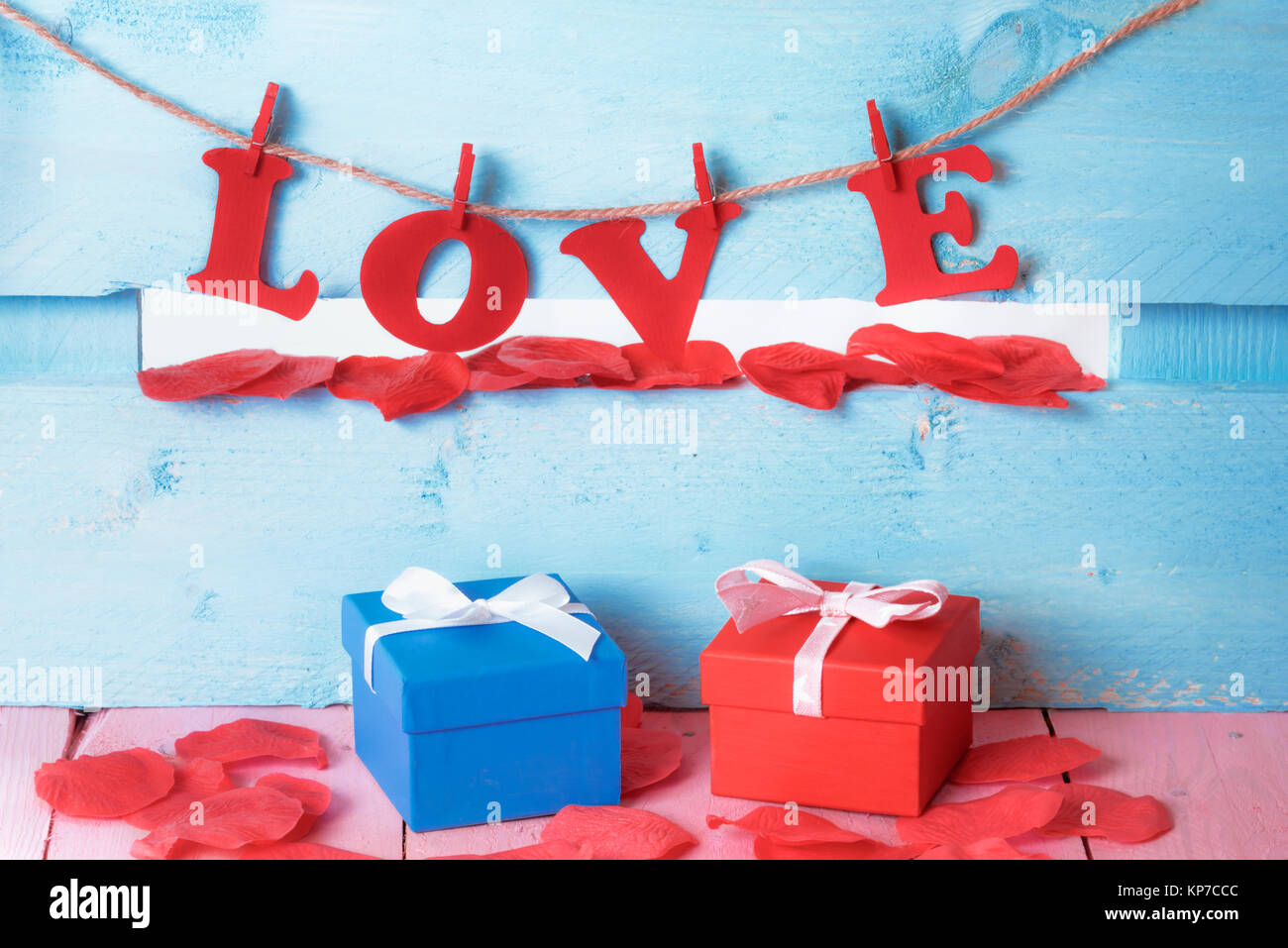 Di lui e di lei confezioni regalo circondato da sapone petali di colore rosso e la parola amore scritto con carta rossa lettere legata a una stringa su un blu staccionata in legno. Foto Stock
