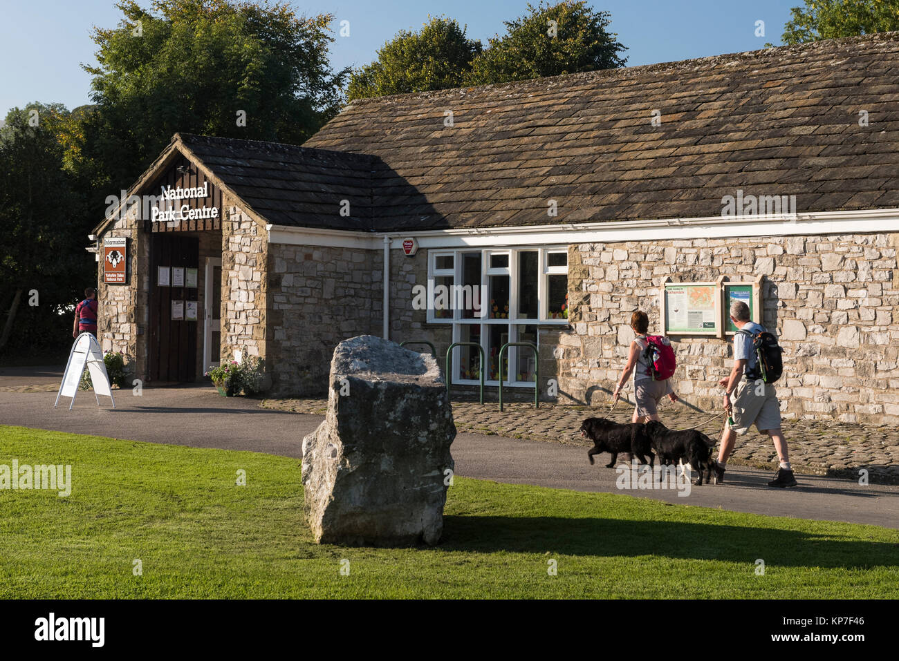 Soleggiato, giornata autunnale, vista esterna del Centro Visitatori del Parco Nazionale, con coppia di camminatori e 2 cani, passando - Malham, Yorkshire Dales, Inghilterra, Regno Unito. Foto Stock