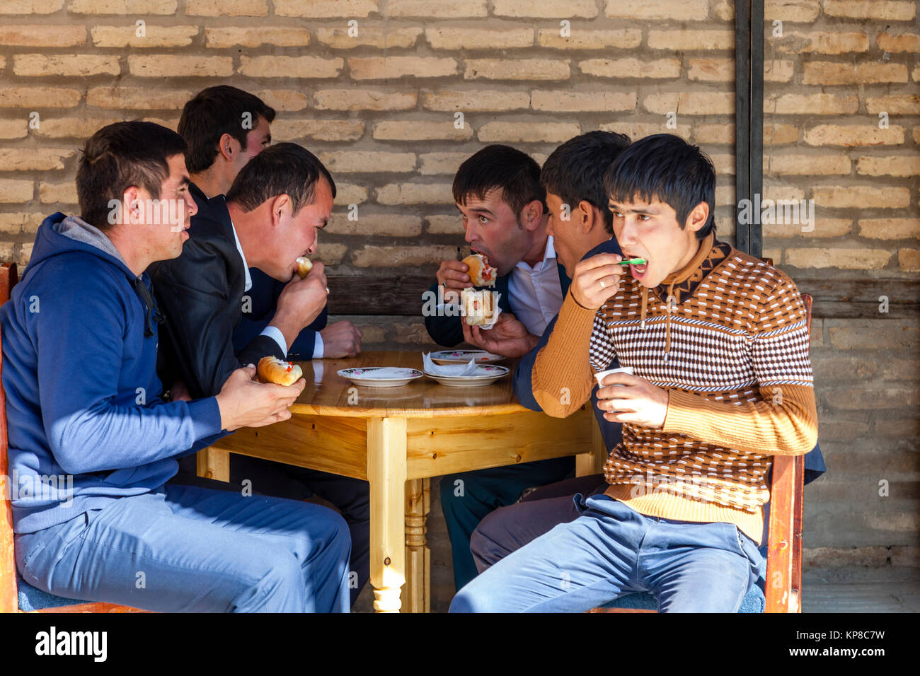 Un gruppo di uomini uzbeki mangiare Hot Dogs al di fuori di un Cafe, Khiva, Uzbekistan Foto Stock