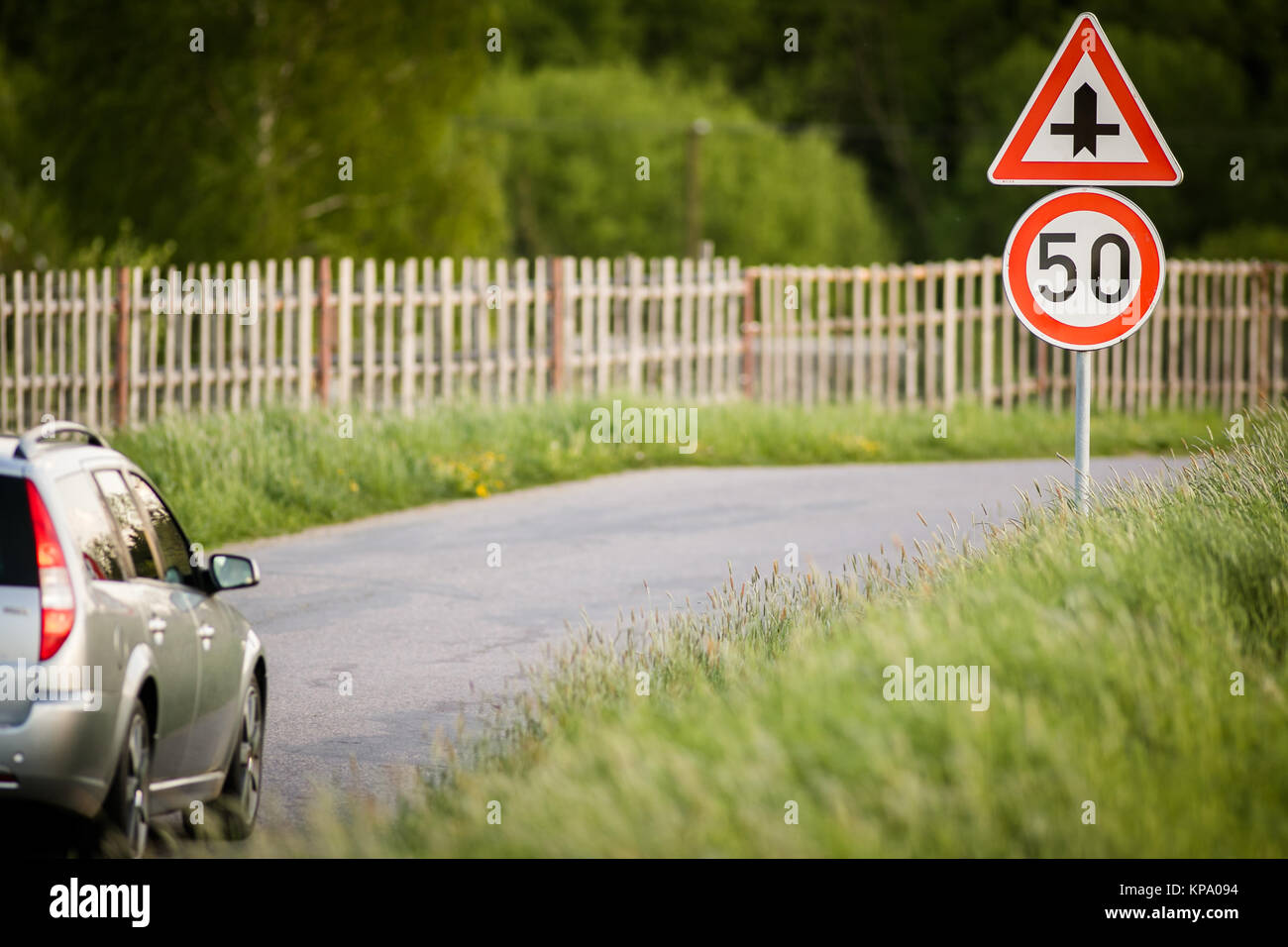 Auto sulla strada di un paese con una velocità limitata e il bivio segno Foto Stock