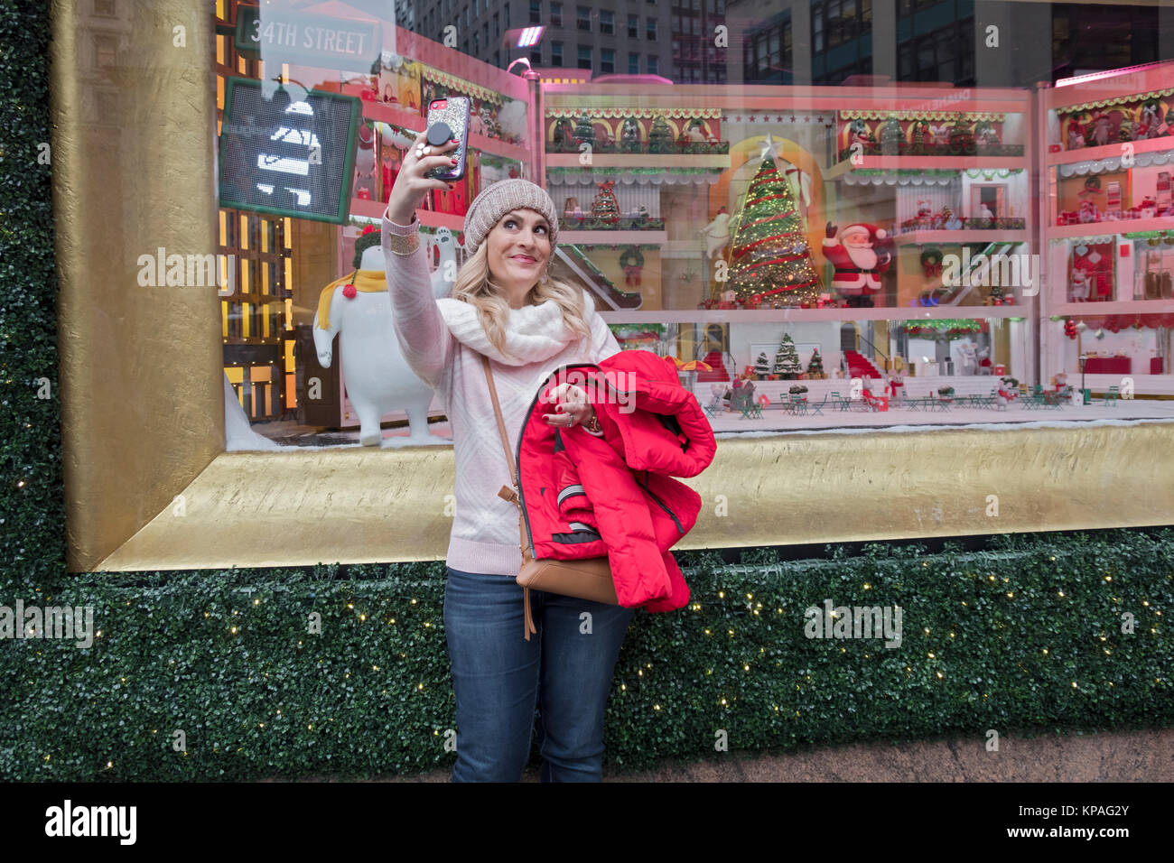 Una bella donna turistica prendendo un selfie davanti a Macy's finestra di Natale in Piazza Herlad a Manhattan, New York City. Foto Stock