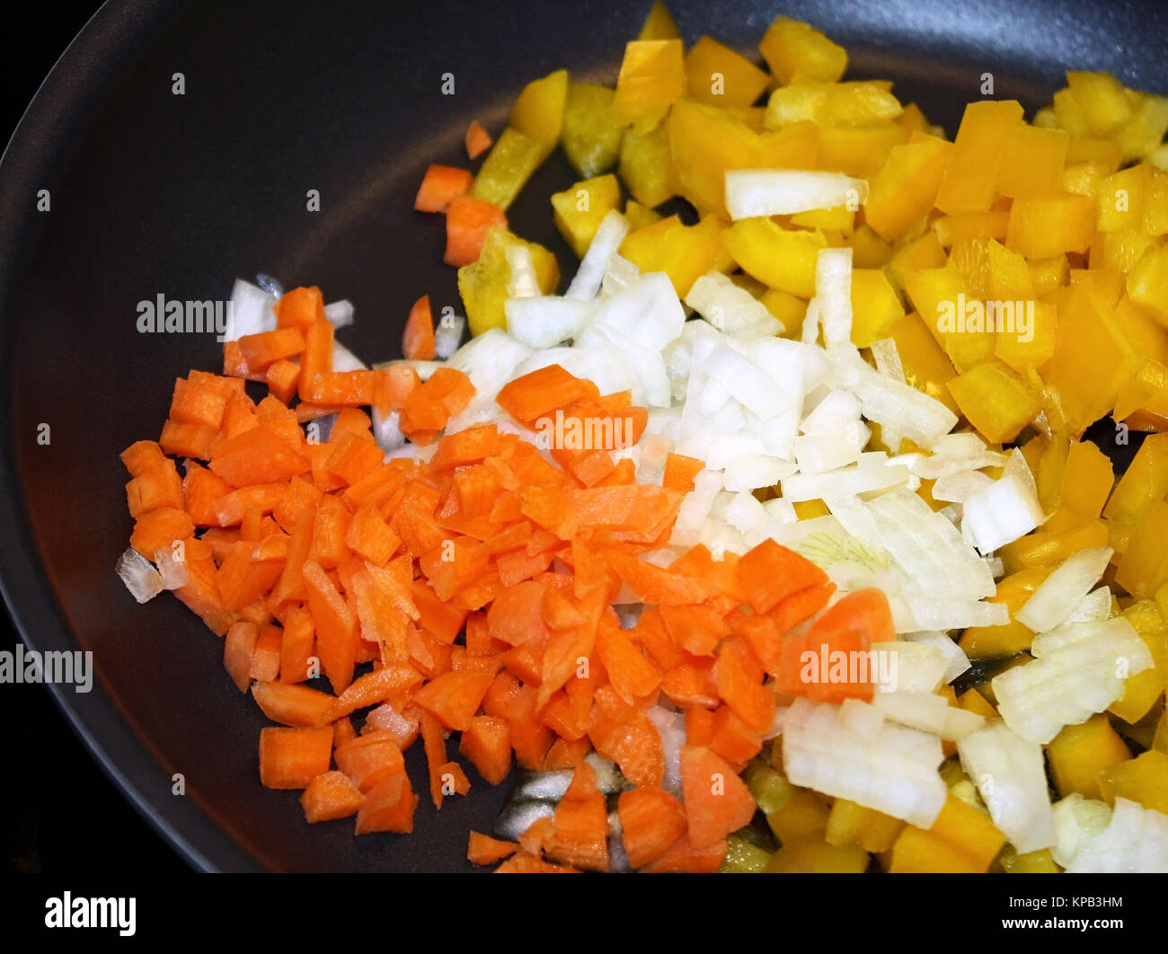 Tagliate a dadini materie carote, cipolle bianche e peperoni gialli in antiaderente padella pronti per la cottura Foto Stock