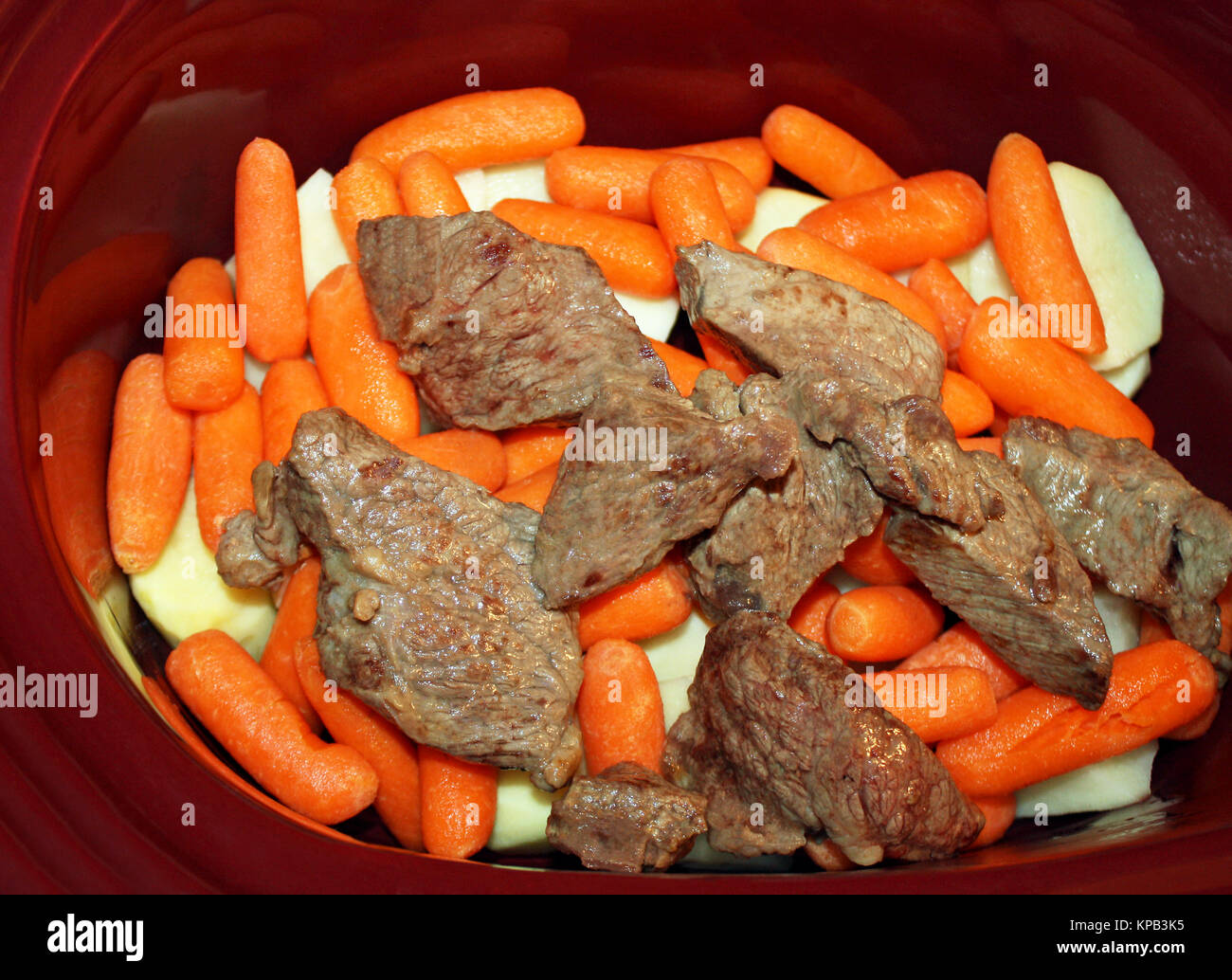 Strati di fettine di patate bianche, pelati mini baby carote e rosolato cottura carni bovine in uno slow cooker Foto Stock