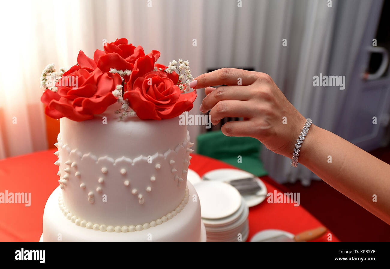Chiudere fino in rosso e bianco torta di nozze e la donna la mano toccando i fiori su di esso Foto Stock