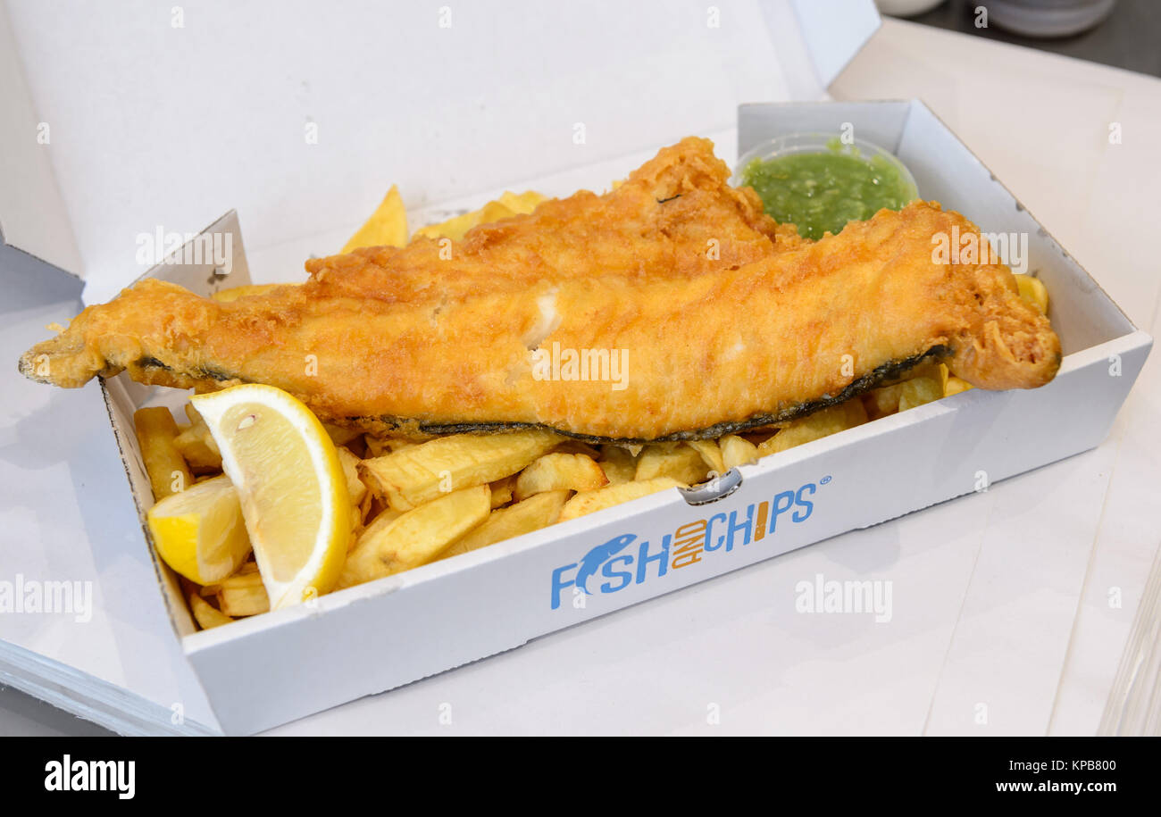 Una grande porzione di pesce tradizionale britannico e patatine con piselli funghi in una scatola. Foto Stock