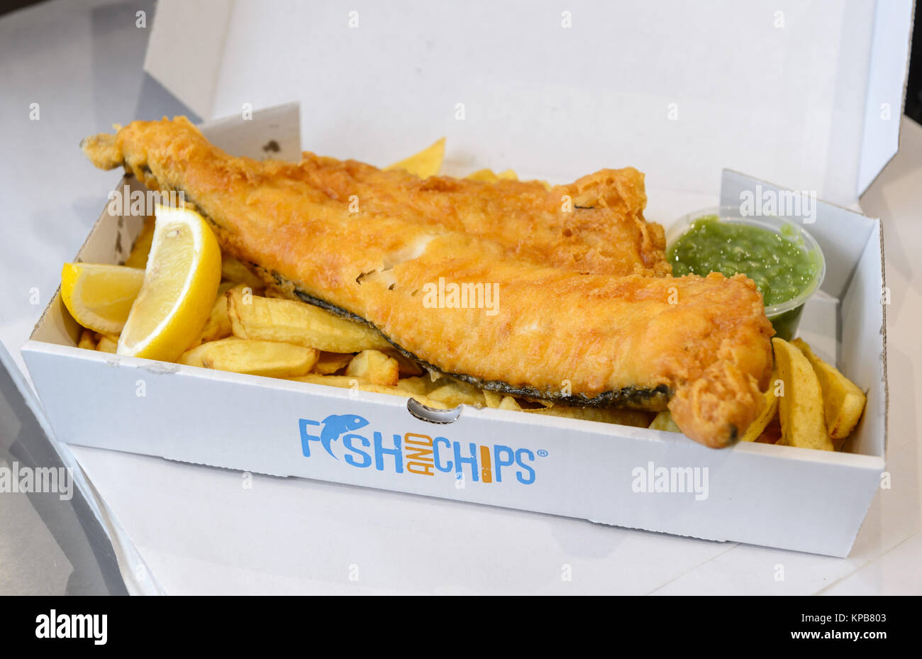 Una grande porzione di pesce tradizionale britannico e patatine con piselli funghi in una scatola. Foto Stock