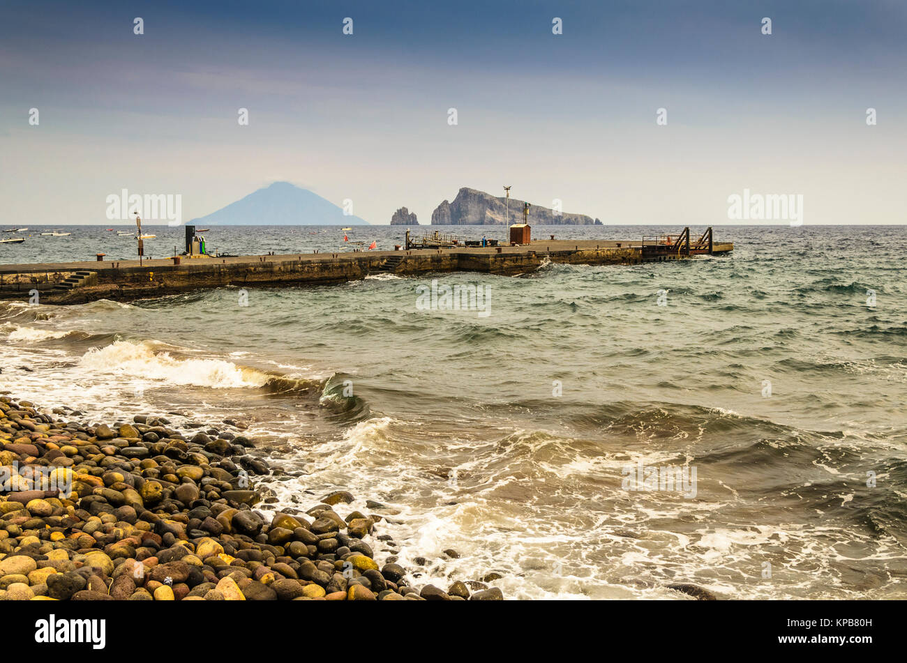 Costa rocciosa imbarco molo dell'isola di Panarea e sullo sfondo il vulcano Stromboli e due scogli emergenti dal Mar Tirreno Foto Stock