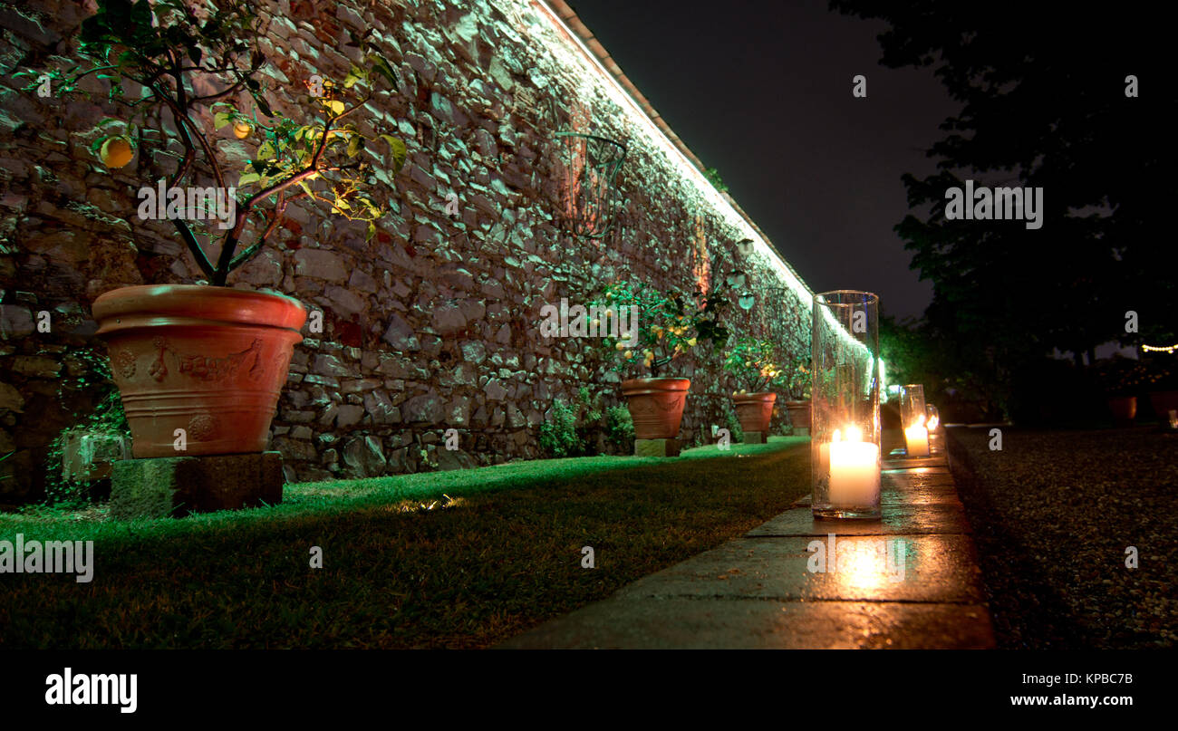 Le candele accese segnano il percorso nel giardino lungo un antico muro di pietra Foto Stock