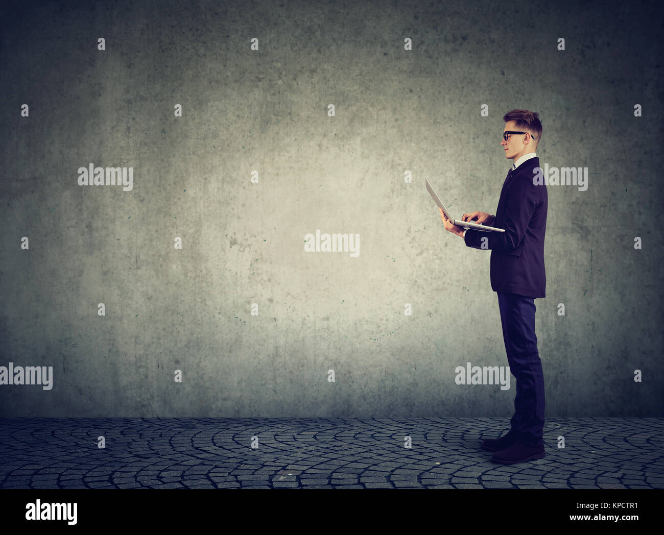 Vista laterale dell'uomo indossare tuta di classe e la navigazione portatile in piedi su sfondo grigio. Foto Stock