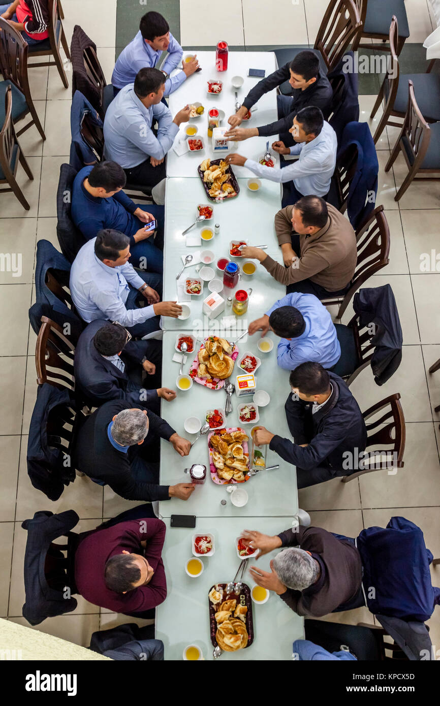 Un grande gruppo di uomini uzbeki mangiare PLOV (il piatto nazionale) presso l'Asia Centrale del centro di Plov, Tashkent, Uzbekistan Foto Stock