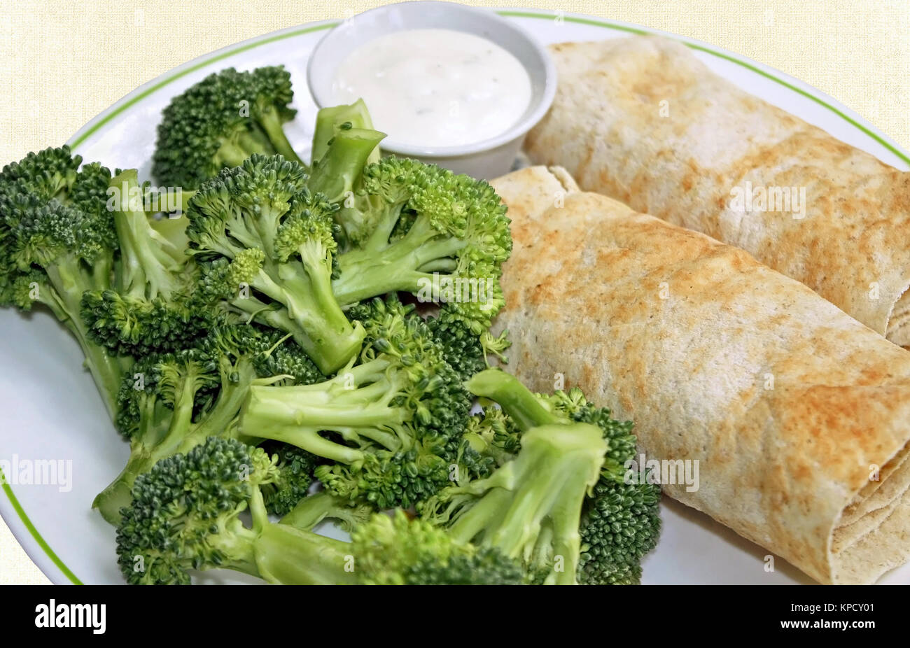 Due riempito tortilla avvolge con un lato di broccoli freschi e un contenitore di condimento cremoso per immersione Foto Stock