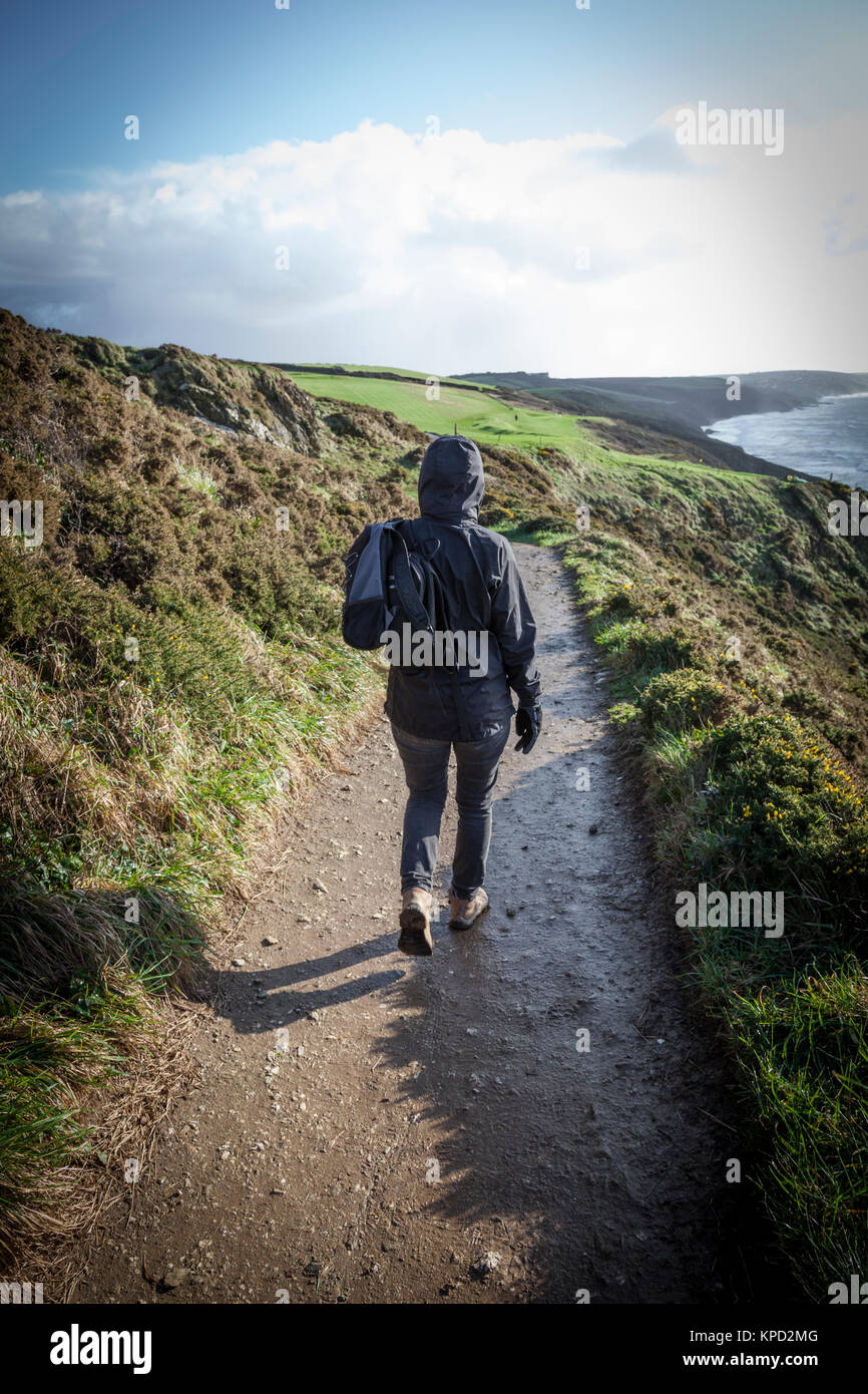 Donna vestita in giacca con cappuccio passeggiate verso est lungo il sud ovest sentiero costiero vicino Portwrinkle, Cornwall. Foto Stock