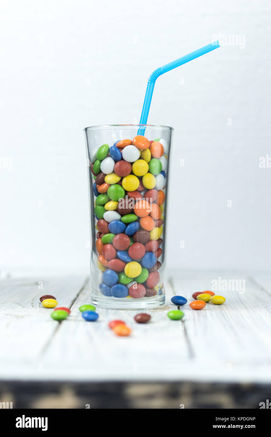 Il vetro è riempita con caramelle colorate. Un bicchiere con un drink e una cannuccia. Caramelle sono sparsi sul tavolo. Foto Stock
