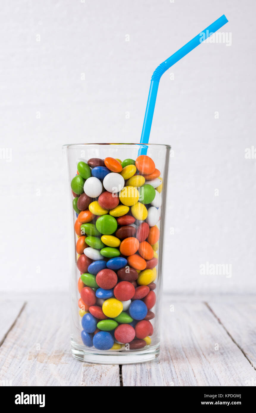Un bicchiere con un drink sul tavolo. Vetro trasparente con un multi-colore confetto. Colpo verticale. Un vetro nel centro. Foto Stock