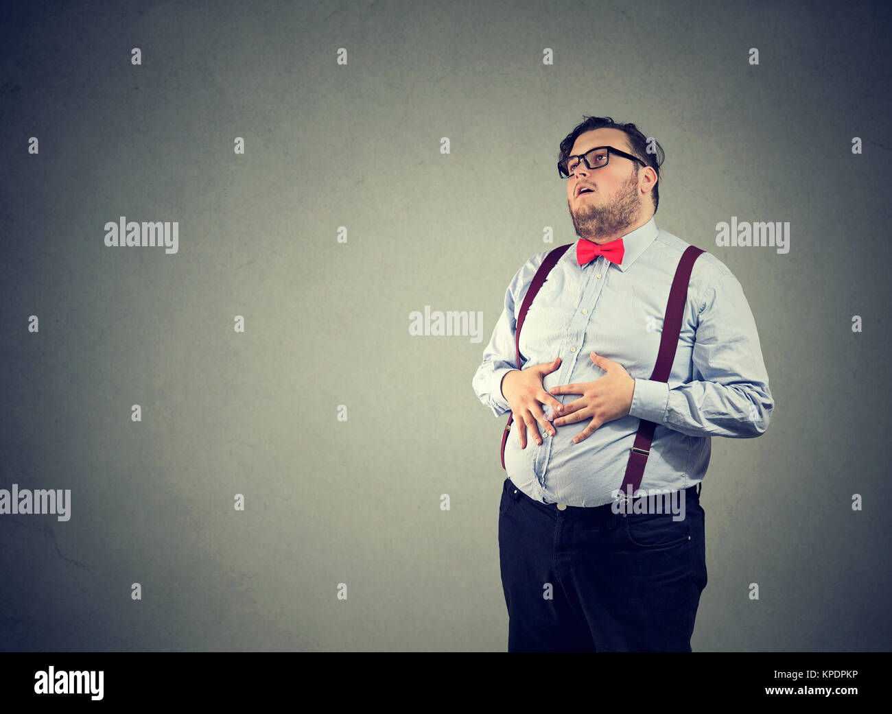 Irritato uomo con il sovrappeso indossando occhiali e abbigliamento formale avente problemi digestivi. Foto Stock
