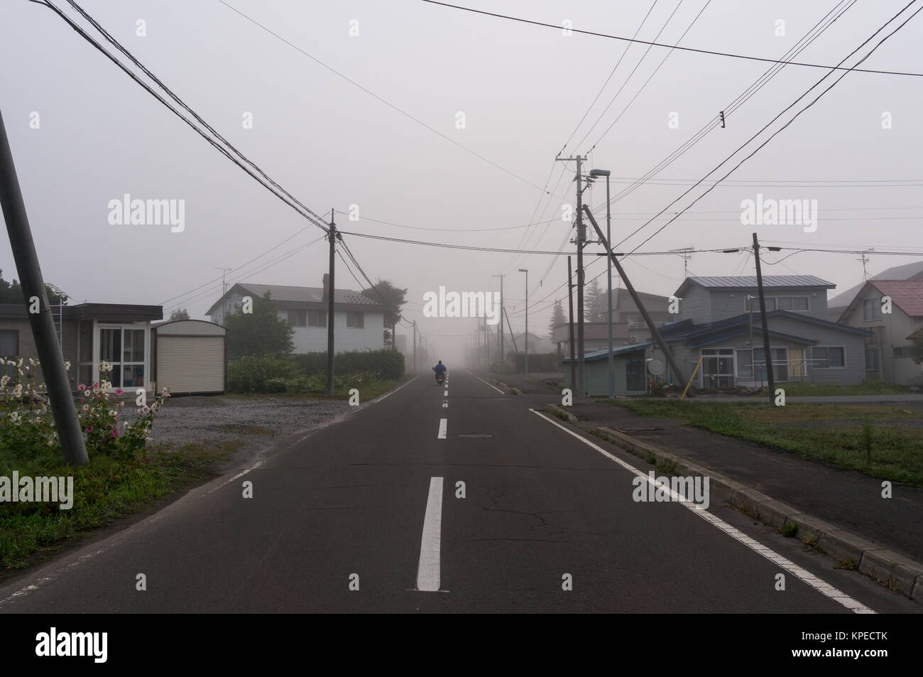 Un motociclista in sella nella nebbia mattutina nel tranquillo paese giapponese di lato Foto Stock