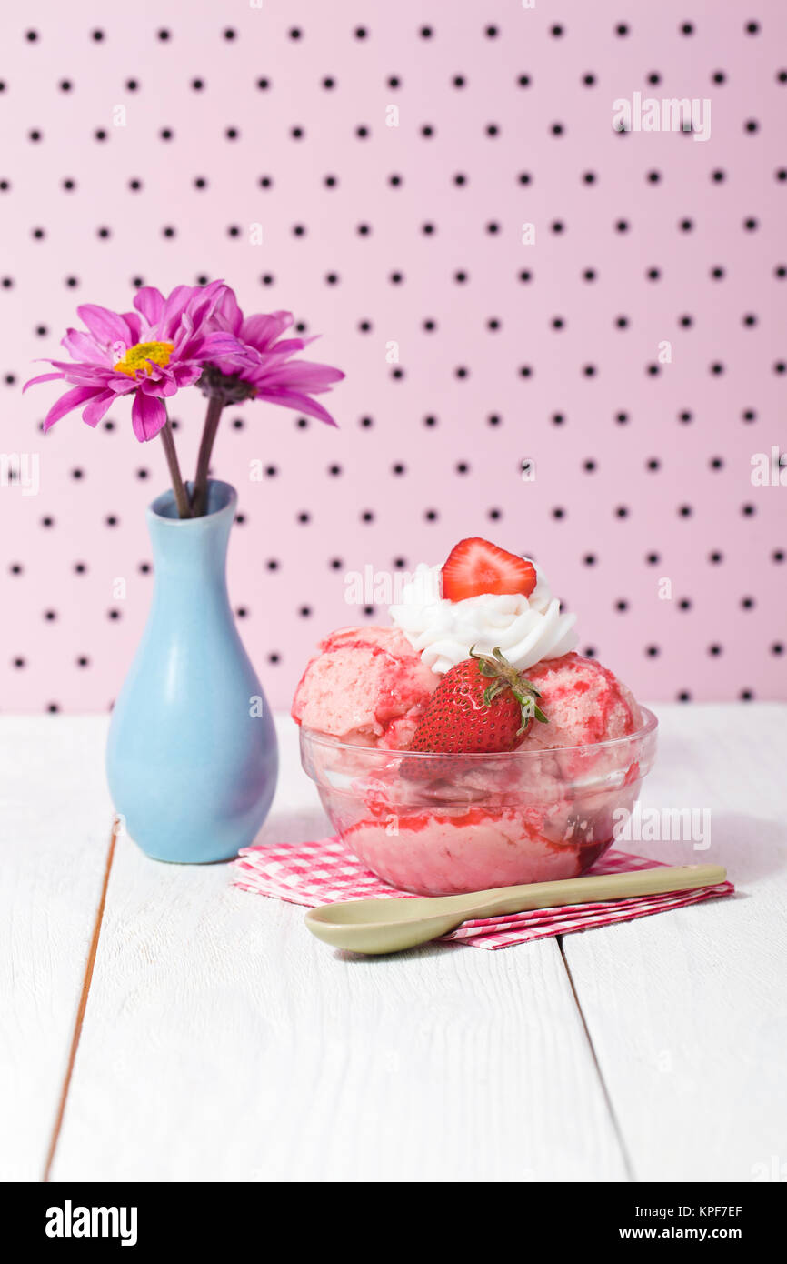 Gelato alla fragola con igienico e cucchiaio accanto a base di fiori Foto Stock