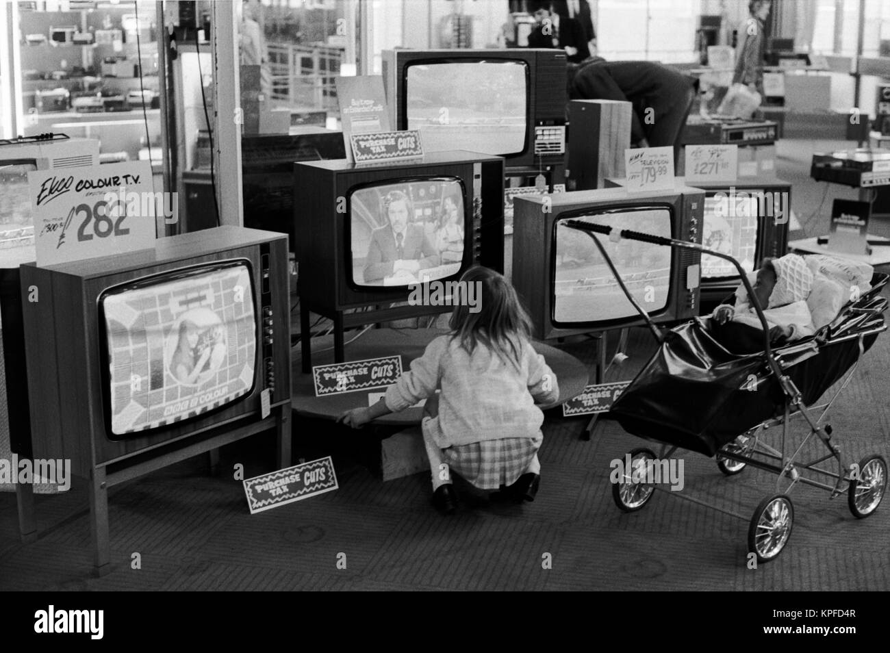 Diversità etnica anni '70 Regno Unito, nero britannico bambino in pram spinto intorno grande magazzino da bianco sorella maggiore Londra anni '70 1972 Regno Unito. I segnali dicono 'tagli fiscali di acquisto'. Dickie Davies il presentatore di ITV World of Sport TV è sul telly. HOMER SYKES Foto Stock
