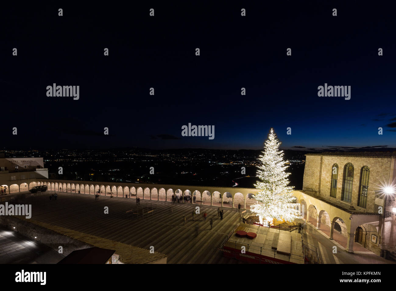 Natale 2017 in Assisi, con una veduta di San Francesco chiesa papale square di notte, con un grande albero illuminato, persone , al di sopra di una vista della valle Umbra Foto Stock