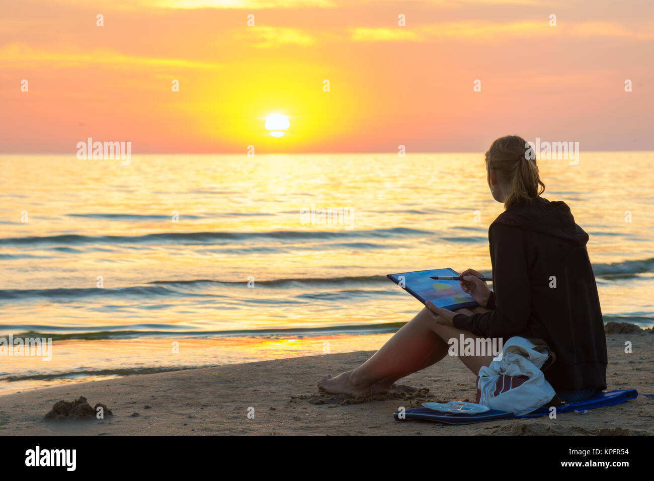 Giovane ragazza seduta sulla spiaggia disegno su di un foglio di acquerello tramonto e guard²