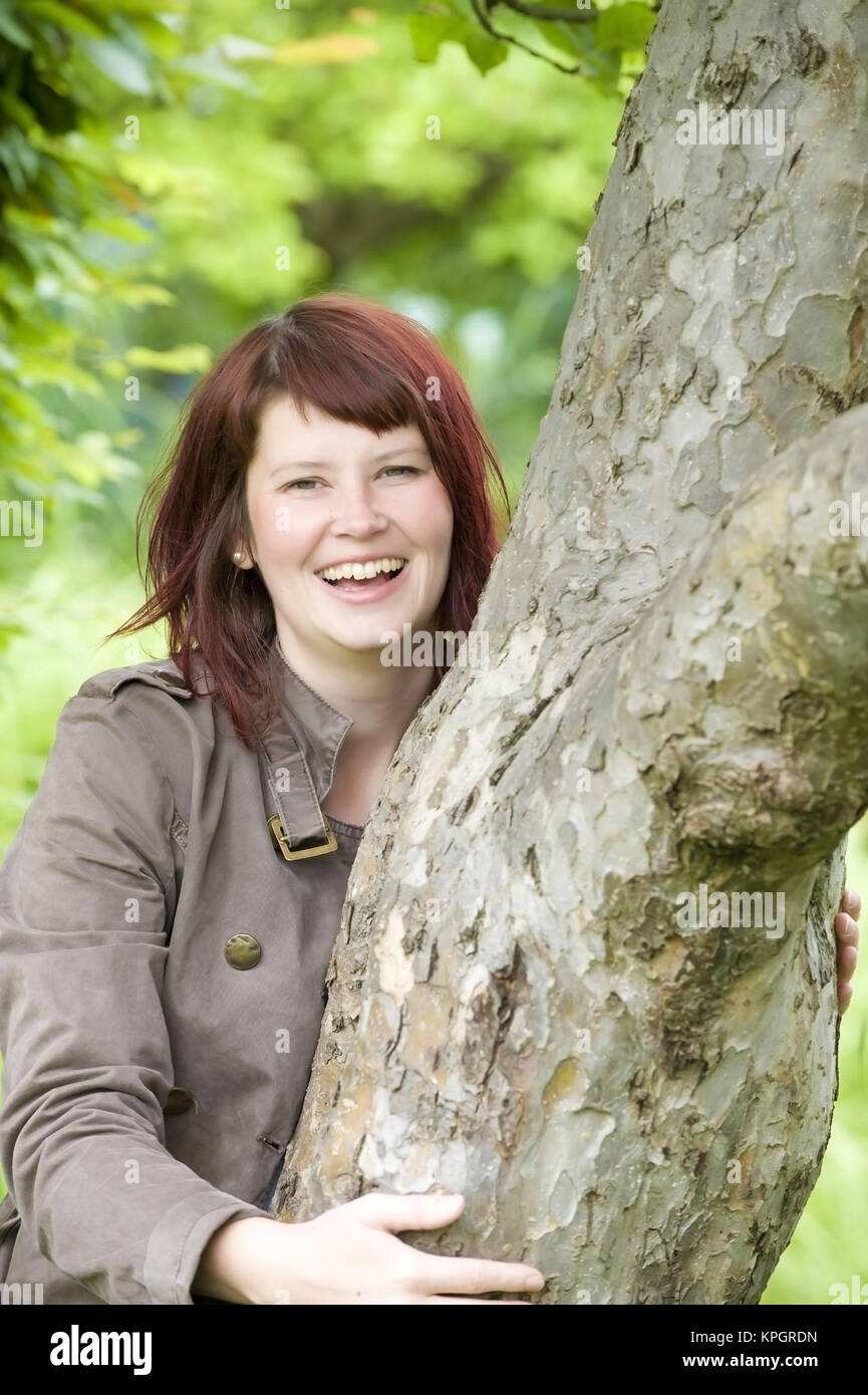 Modello rilasciato , Froehliche Frau, 25+, umgreift einen Baumstamm - lucky donna accanto a un albero Foto Stock