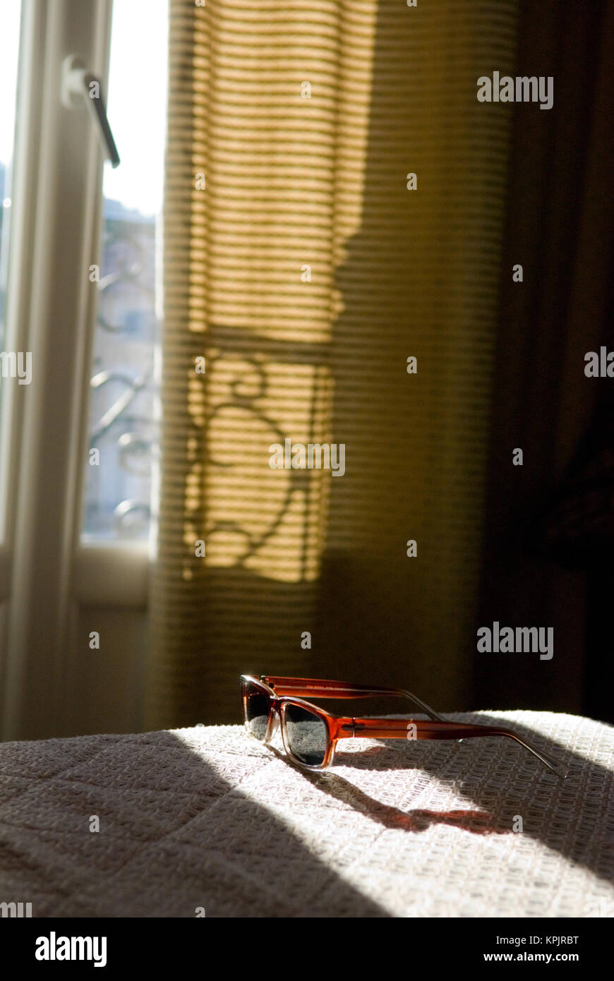 Sun striature attraverso una finestra di hotel su occhiali da sole giacente su un letto di reso Foto Stock