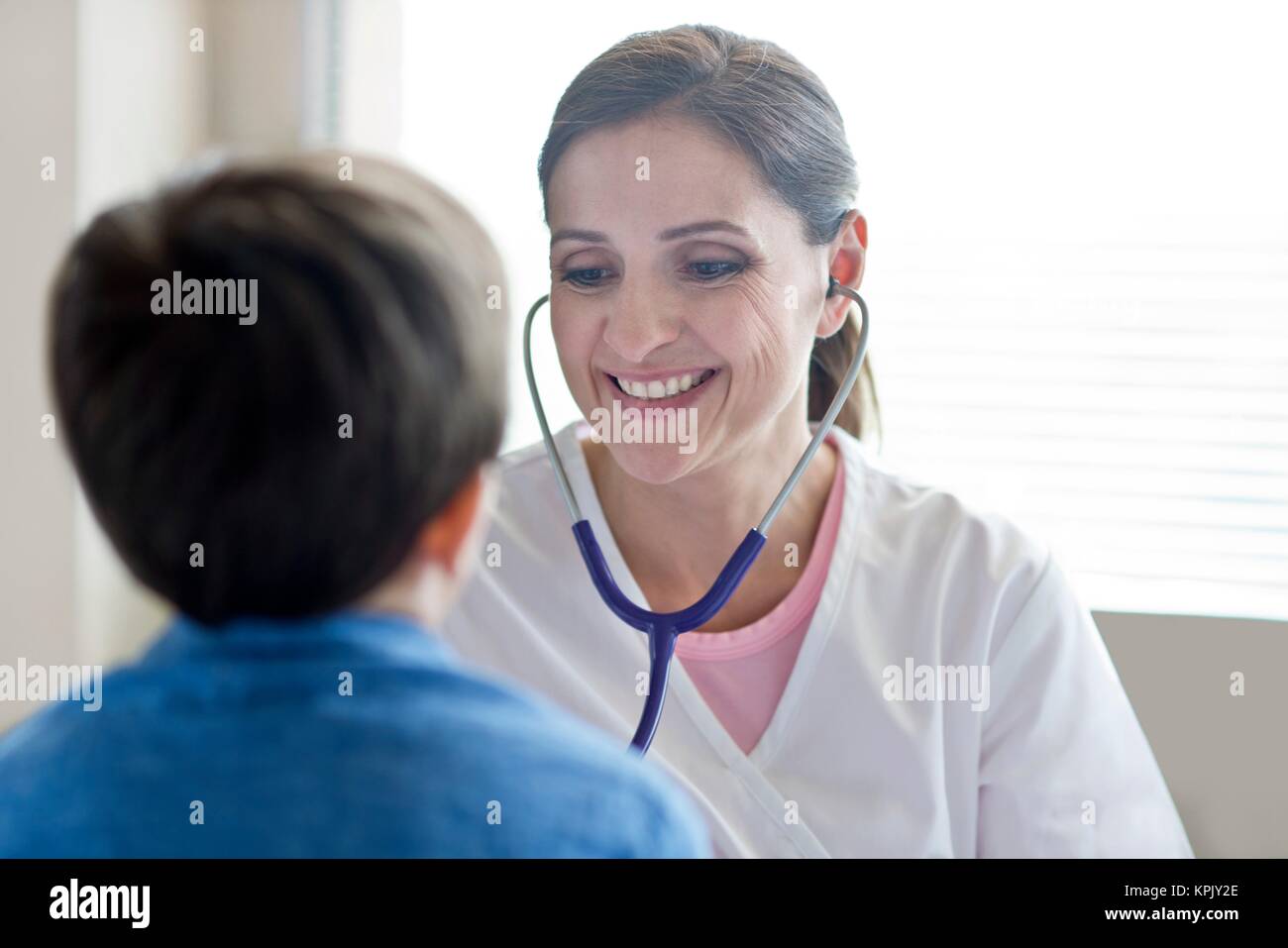 L'infermiera utilizzando uno stetoscopio, sorridente verso il ragazzo. Foto Stock