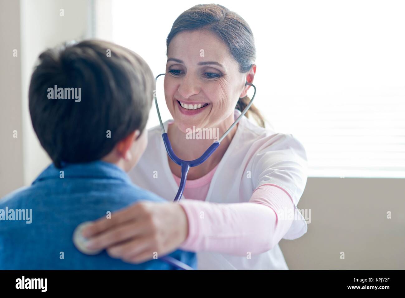L'infermiera utilizzando uno stetoscopio, sorridente verso il ragazzo. Foto Stock