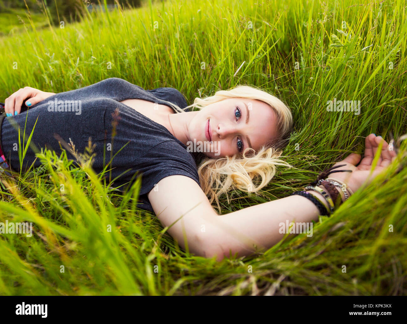 Ritratto di una giovane donna con capelli lunghi biondi posa sull'erba in un parco; Edmonton, Alberta, Canada Foto Stock