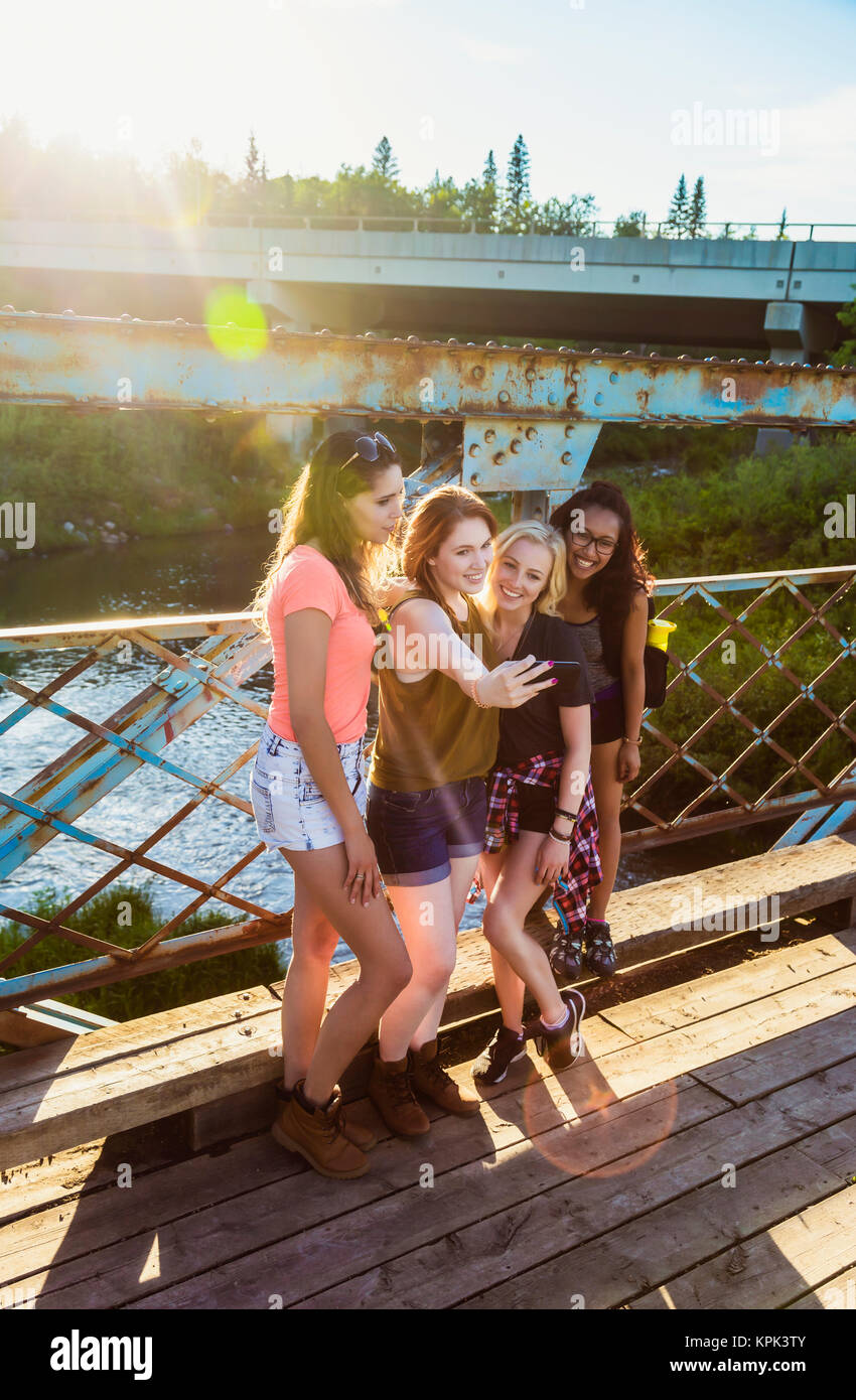 Un gruppo di quattro amiche posare per un autoritratto con uno smart phone su un ponte in un parco; Edmonton, Alberta, Canada Foto Stock