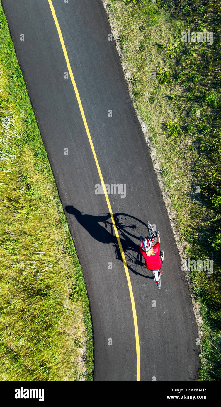 Vista da direttamente al di sopra di un ciclista in una maglietta rossa su un lastricato sentiero ciclabile; Calgary, Alberta, Canada Foto Stock