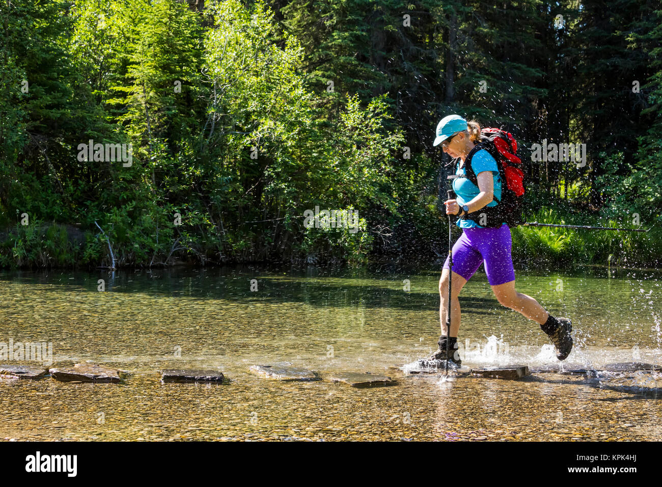 Una femmina di un escursionista con pali trekking salti di roccia in roccia in un flusso poco profonde e spruzzi di acqua con i suoi stivali; Calgary, Alberta, Canada Foto Stock