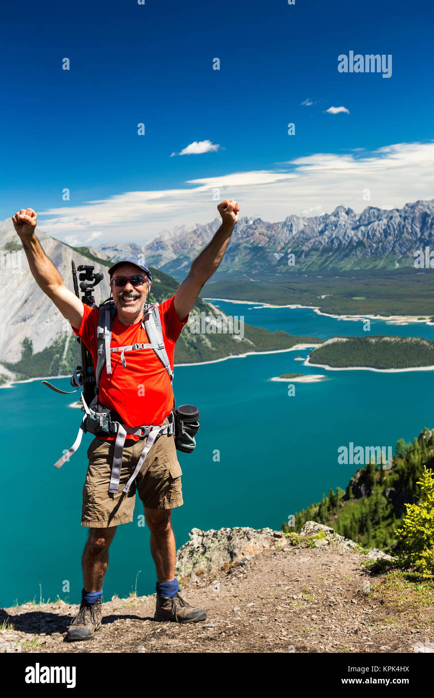 Escursionista femmina sulla cresta del top con le braccia in aria e un colorato lago alpino e la gamma della montagna di distanza con il cielo blu e nuvole Foto Stock