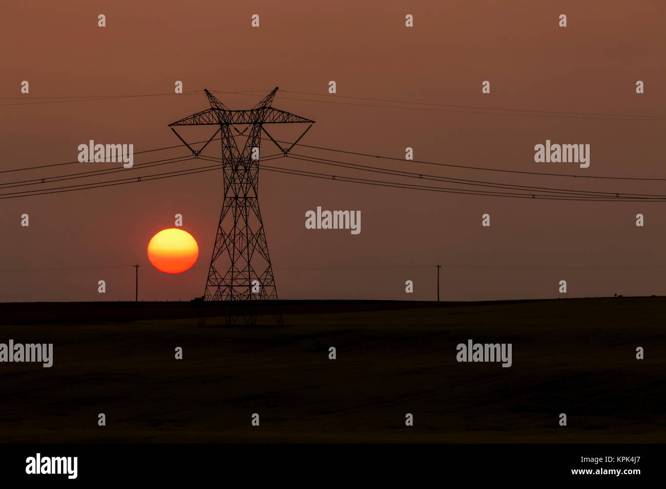 Silhouette di metallo grande torre elettrico con le linee di alimentazione e di sole arancione palla; Blackie, Alberta, Canada Foto Stock