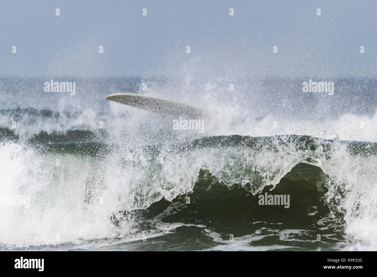 Onde che si infrangono e schiantarsi vicino a riva con una tavola da surf nella gli spruzzi di acqua sulla parte superiore della forma d'onda; Tofino, British Columbia, Canada Foto Stock