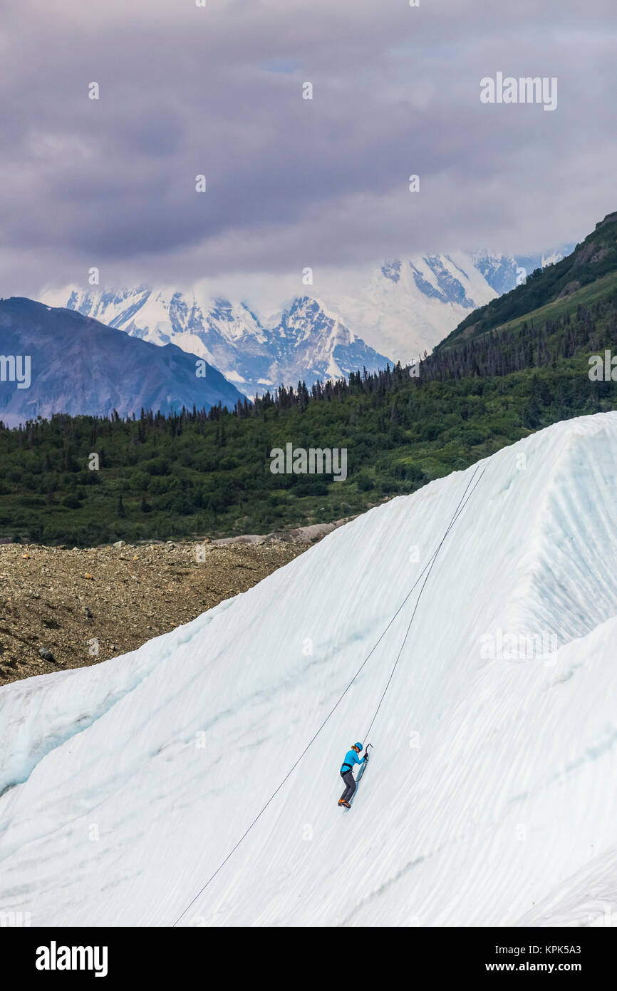 Una donna di ghiaccio si arrampica sul ghiacciaio di radice in Wrangell-St. Elias National Park con Mt. Blackburn in background; Alaska, Stati Uniti d'America Foto Stock