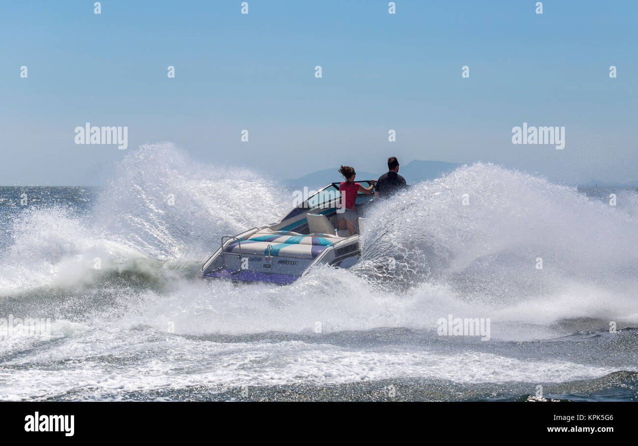 Un motoscafo hits di una grande onda oceanica inviando un enorme splash come il conducente e il passeggero stand a prua guardando avanti Foto Stock