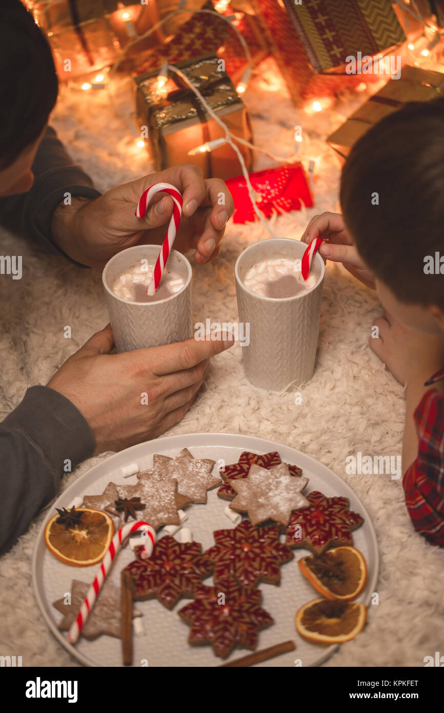 Padre con figlio posa sotto albero di natale con cioccolata e biscotti. Foto Stock