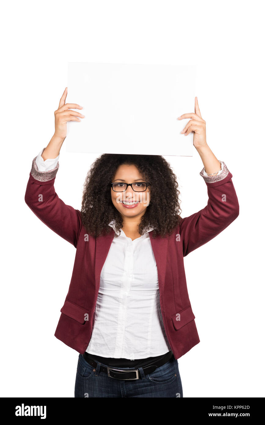 Freigestelltes Foto einer jungen Frau mit dunklen lockigen Haaren (Afro-Look) und Brille, die ein weißes leeres Blatt Papier über dem Kopf hält. Foto Stock