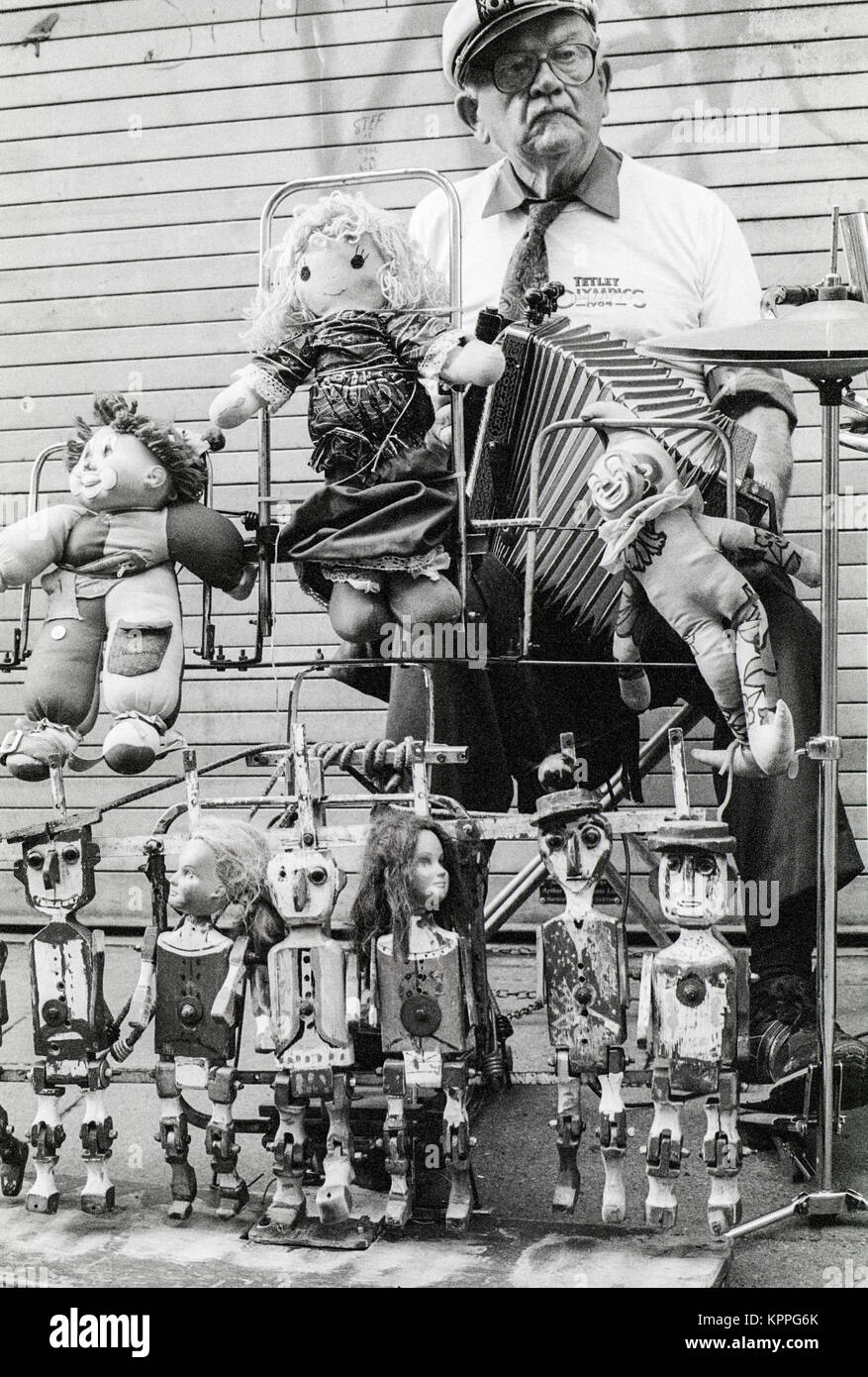 One man band, uomo vecchio con il volto triste e riproduzione di formare fisarmonica e operando una strana impostato con dancing dolls, Dublino, Irlanda. 1989 Foto Stock
