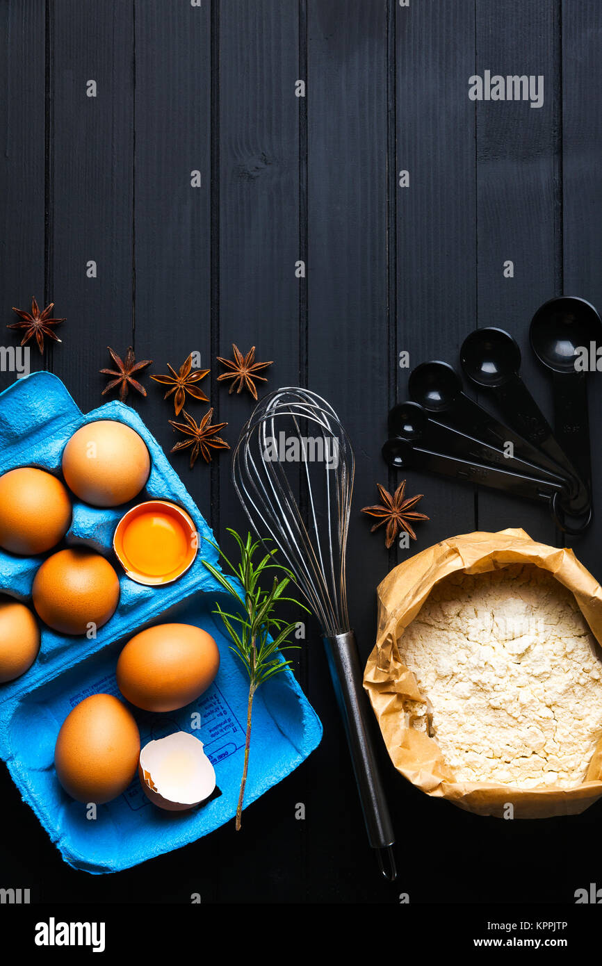 Le uova in una carta blu contenitore , Farina e utensili da cucina per la cottura. Sfondo culinario. tuorlo Foto Stock