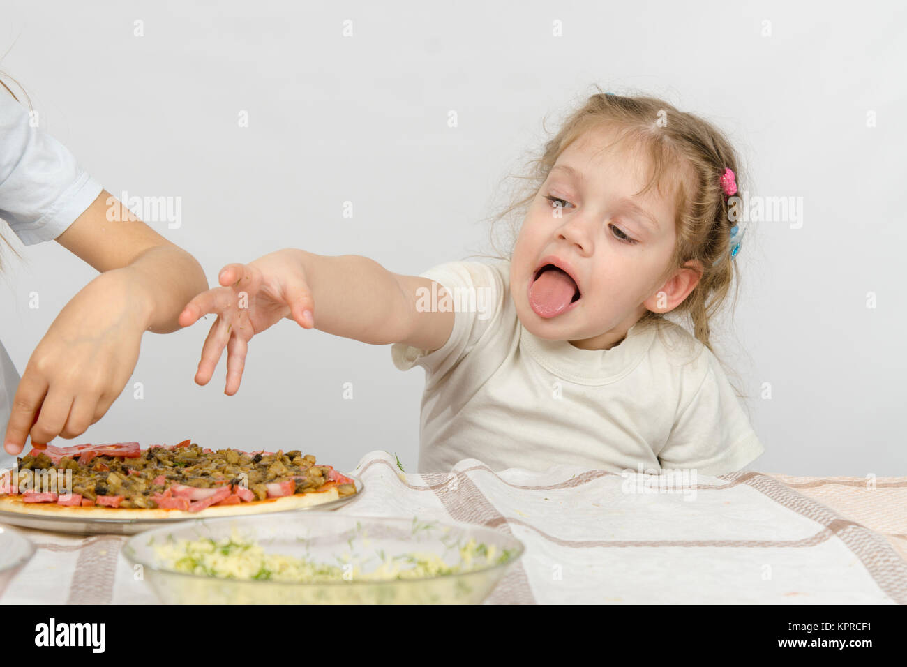 Bambina con la lingua fuori una mano a tirare la pizza, che prepara la sua sorella maggiore Foto Stock