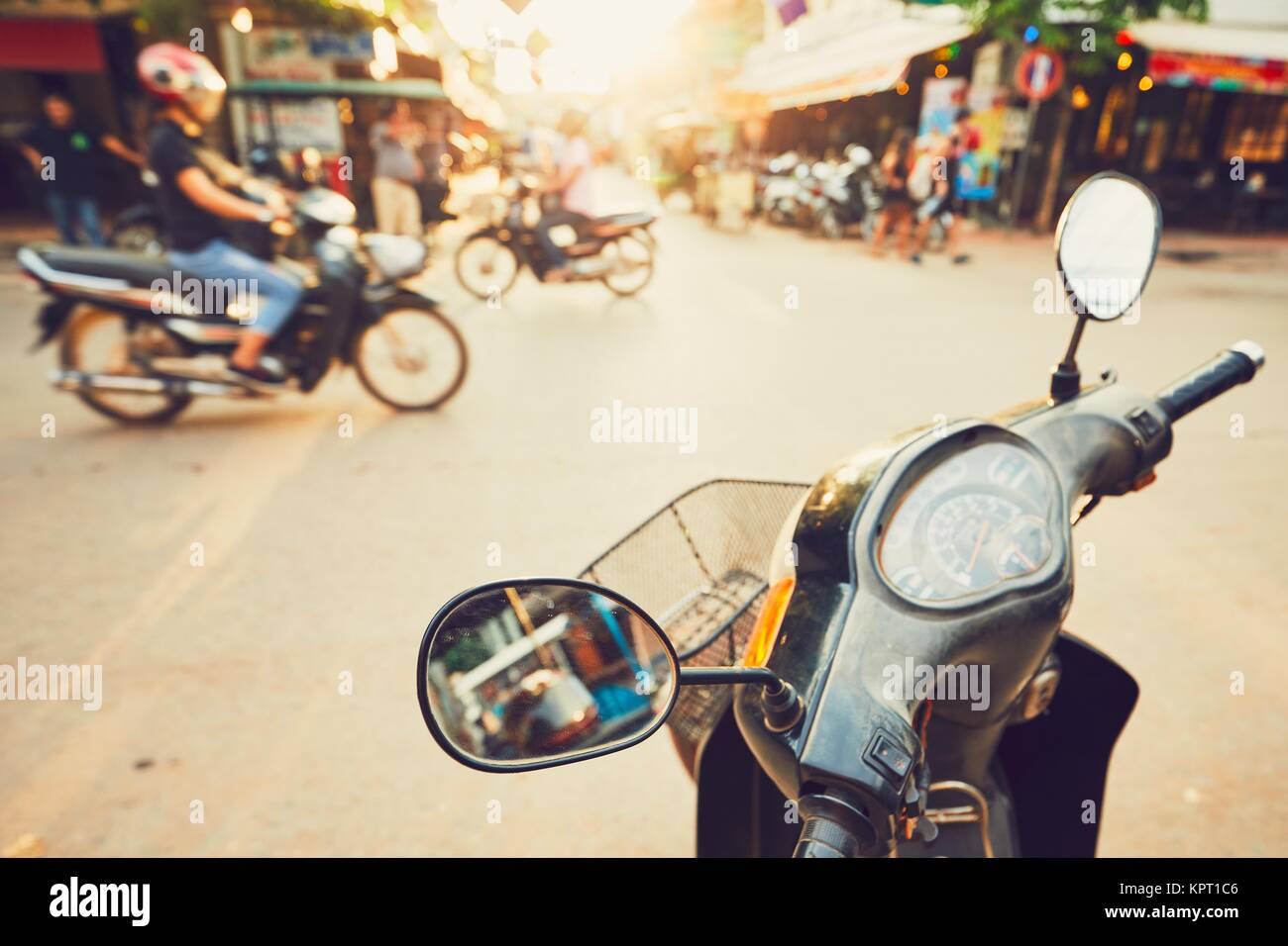 Siem Reap città al tramonto. Il traffico sulla strada trafficata piena di ristoranti, bar e negozi. Messa a fuoco selettiva sullo specchio del ciclomotore. Foto Stock