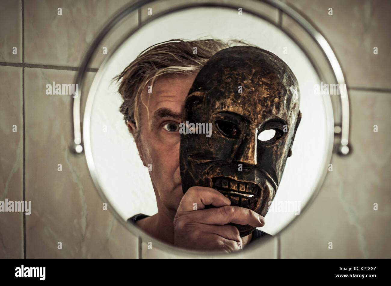 Mann mit Maske betrachtet sich im Spiegel. Foto Stock
