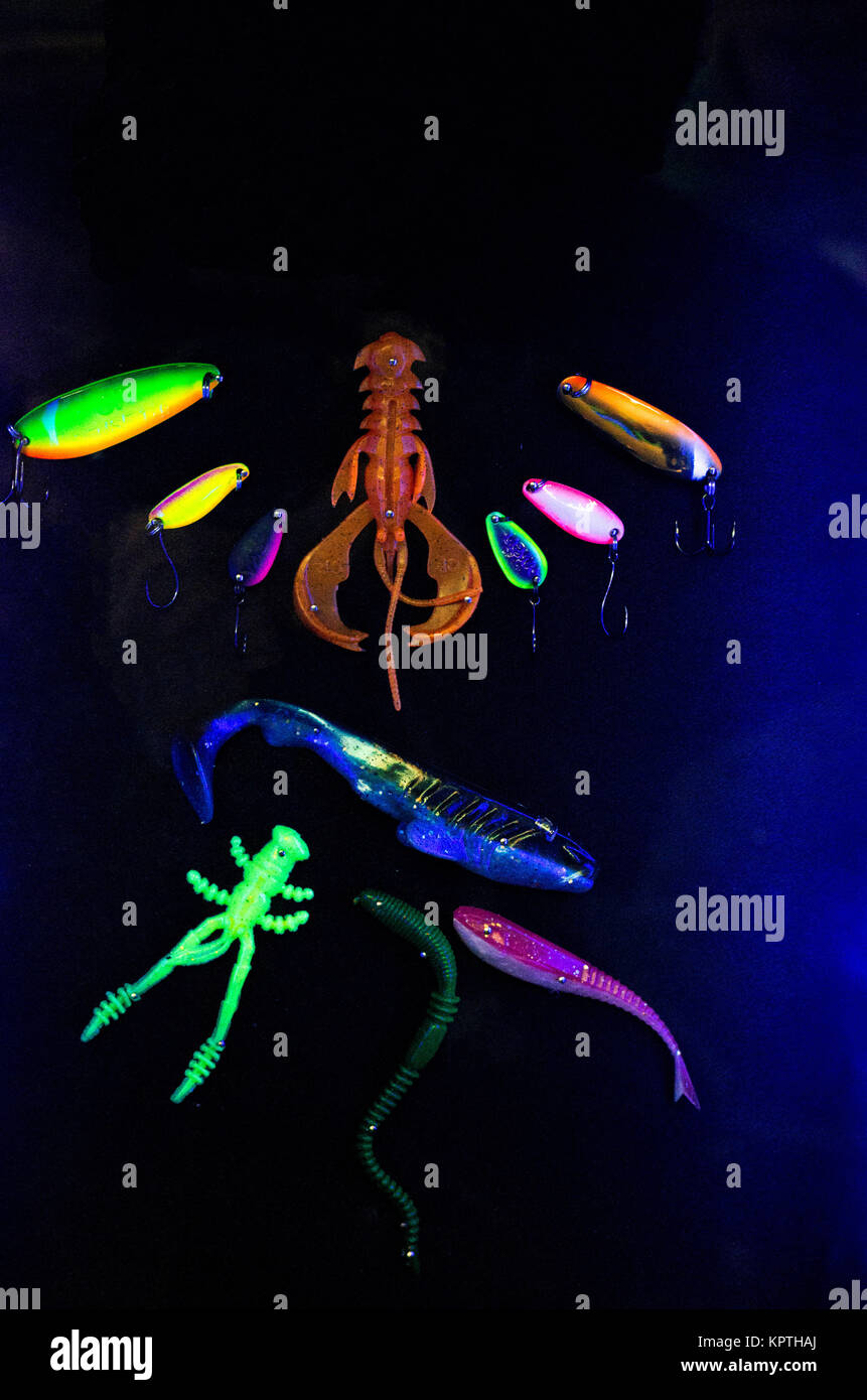 Una varietà di esche soft per la pesca. Esche multicolore. Sfondo nero e luce al neon. Foto Stock