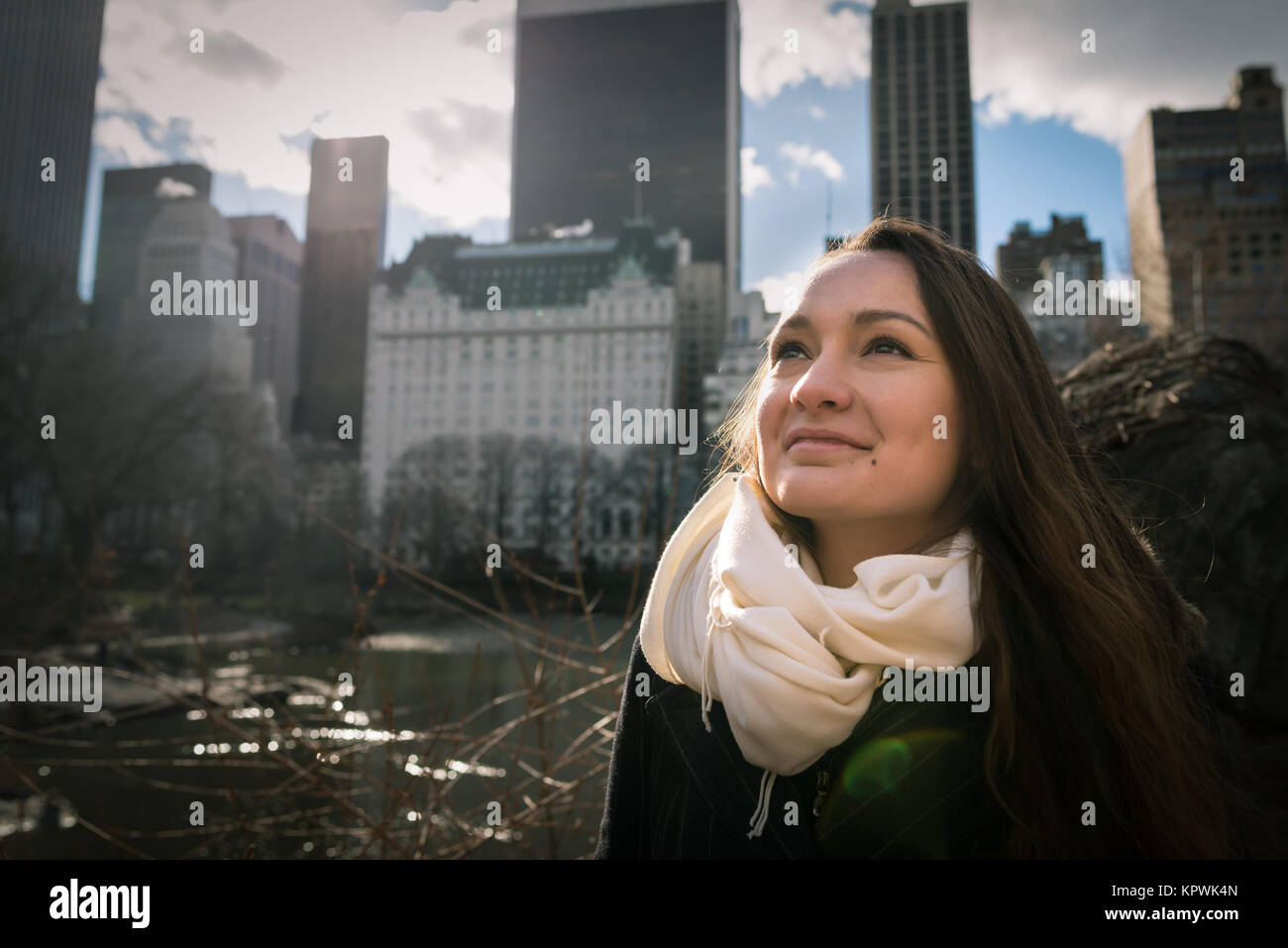 Una giovane donna nelle prime ore del mattino è in piedi nel central Park di New York ed è alla ricerca di distanza sul paesaggio urbano in background. Una persona Foto Stock