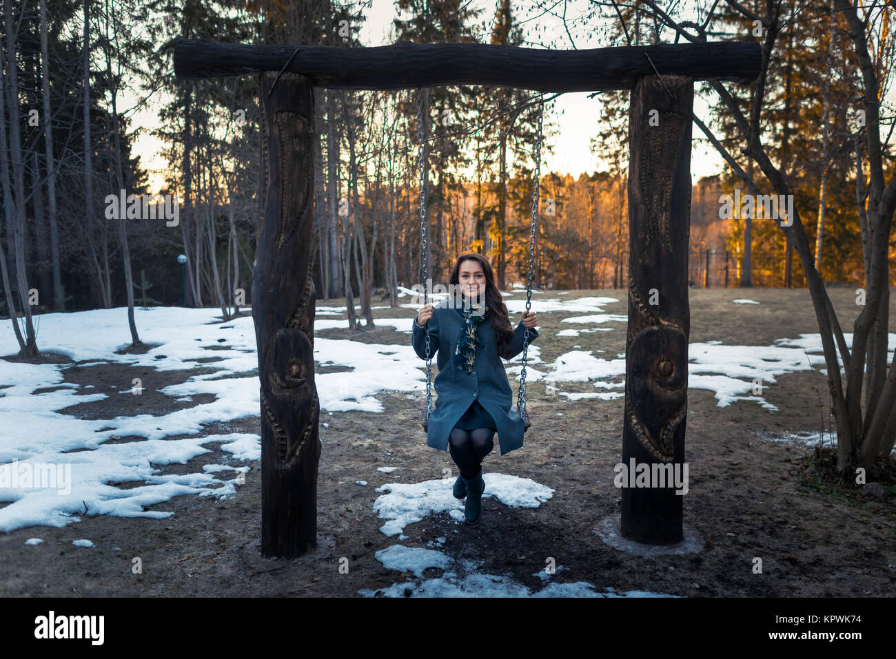 Felice giovane donna basculante in una swing hanno divertimento e sorridente nel parco nella soleggiata giornata invernale Foto Stock