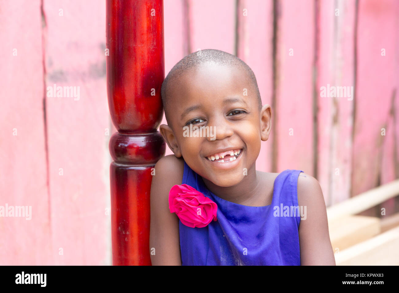 Una bella ugandese ragazza sorridente. Ella è vestito con un abito blu con un fiore rosa su di esso. Foto Stock