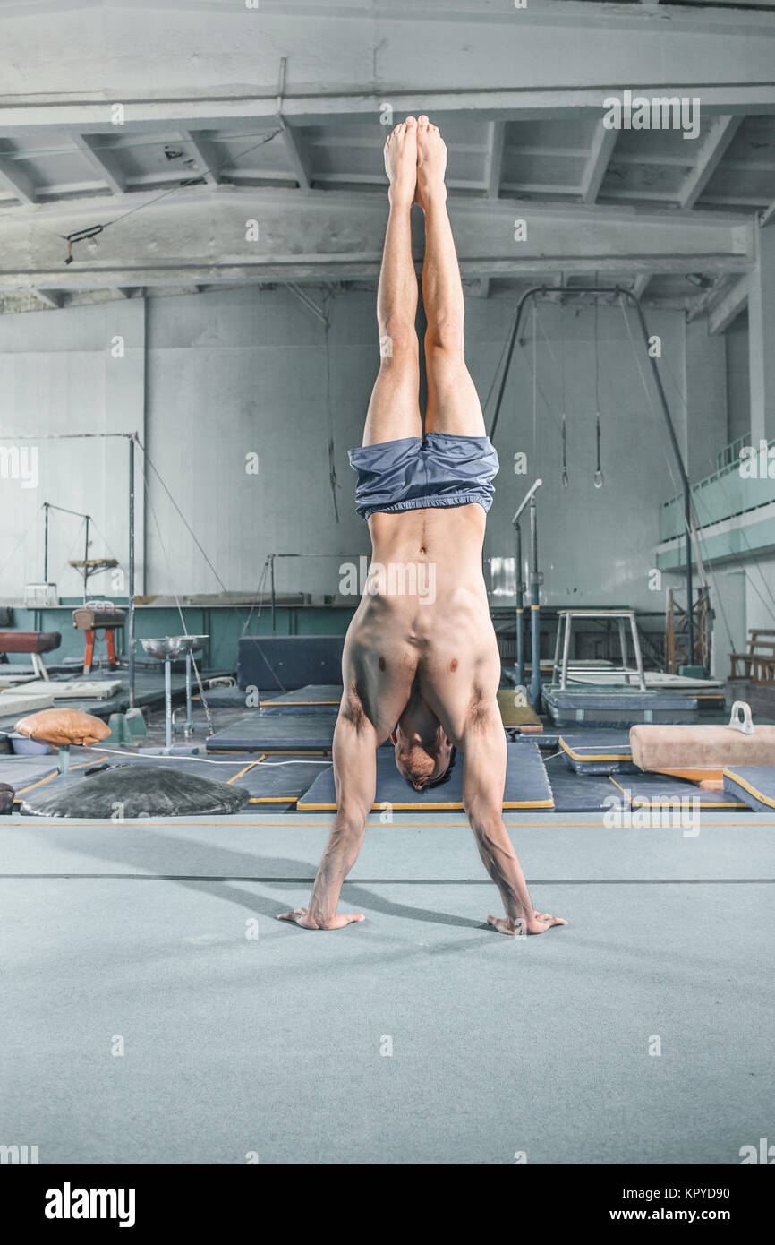Uomo caucasico ginnastica acrobatica postura di equilibrio a sfondo palestra Foto Stock Uomo caucasico ginnastica acrobatica postura di equilibrio a sfondo palestra Foto Stock