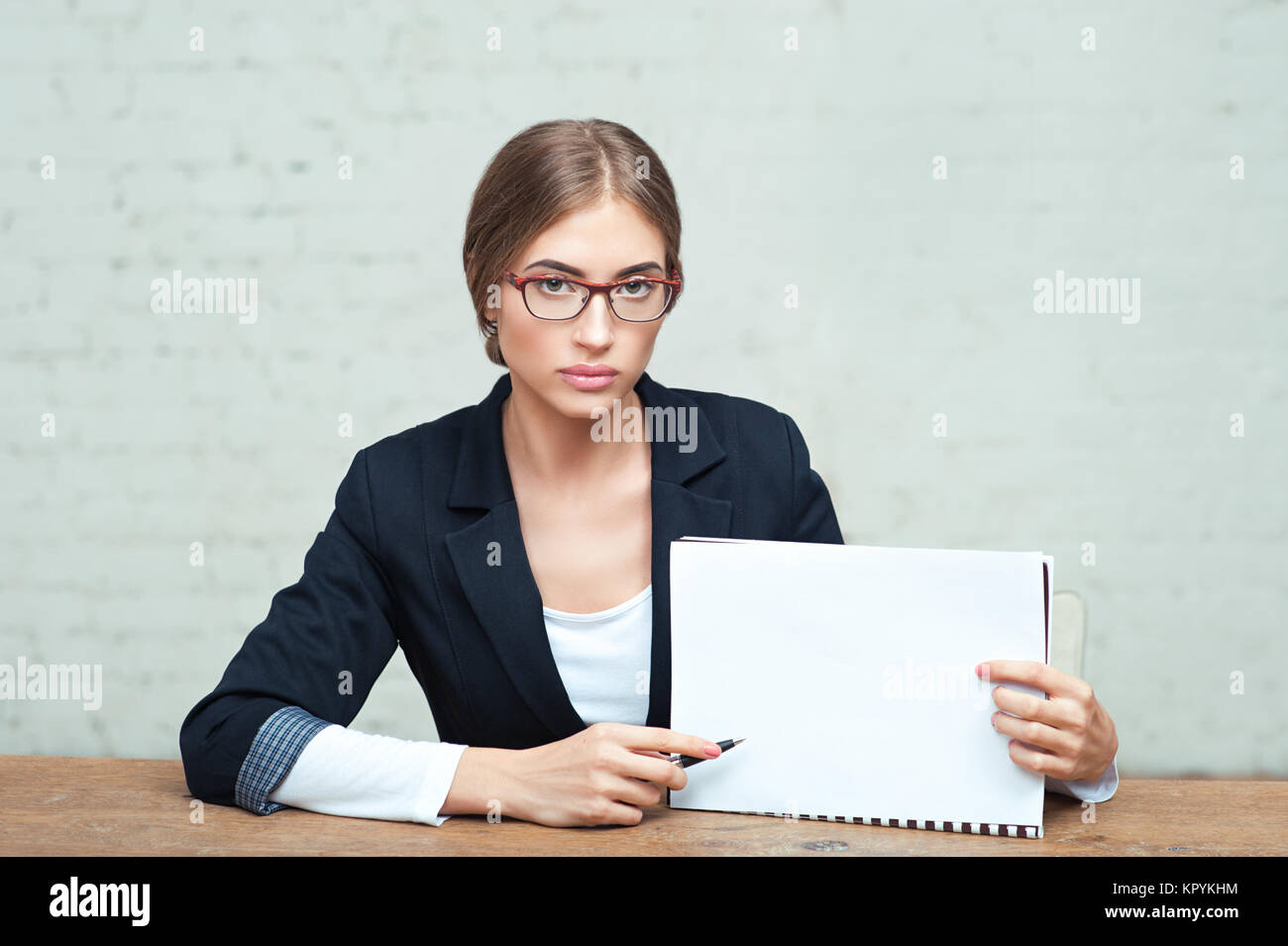 Ritratto di giovane donna d'affari con gli occhiali seduto in ufficio e che mostra blank white paper Foto Stock